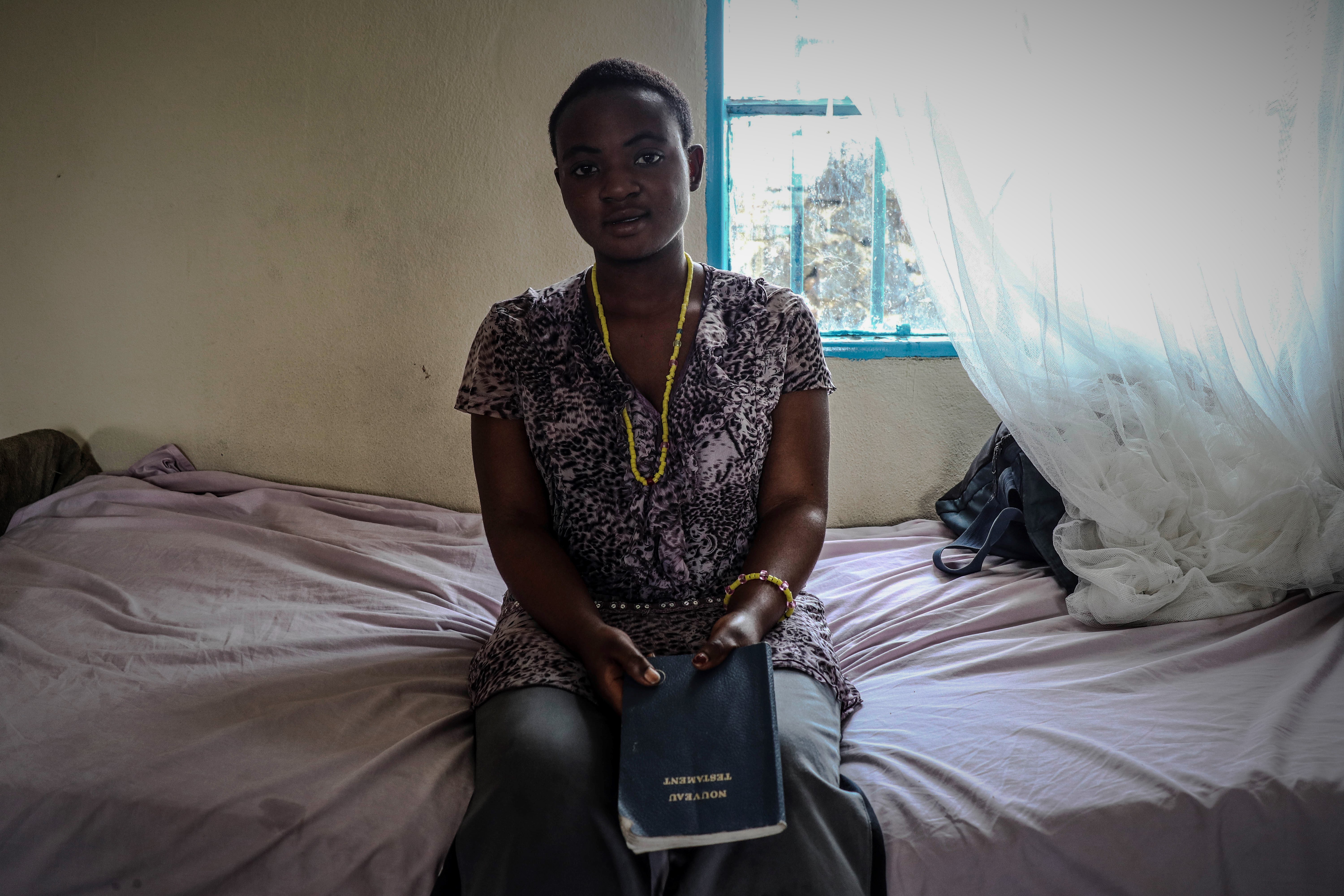 Assise devant son lit, une jeune malade tient une bible. Elle se protège du sort maléfique que sa famille lui aurait jeté