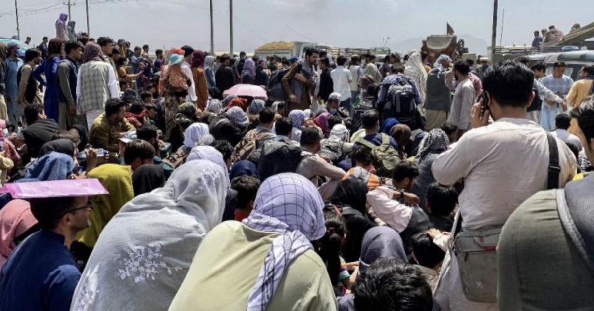 Des Afghans le long d'une route en attendant de monter à bord d'un avion militaire américain pour quitter le pays, à l'aéroport militaire de Kaboul, le 20 août 2021.  (WAKIL KOHSAR / AFP)